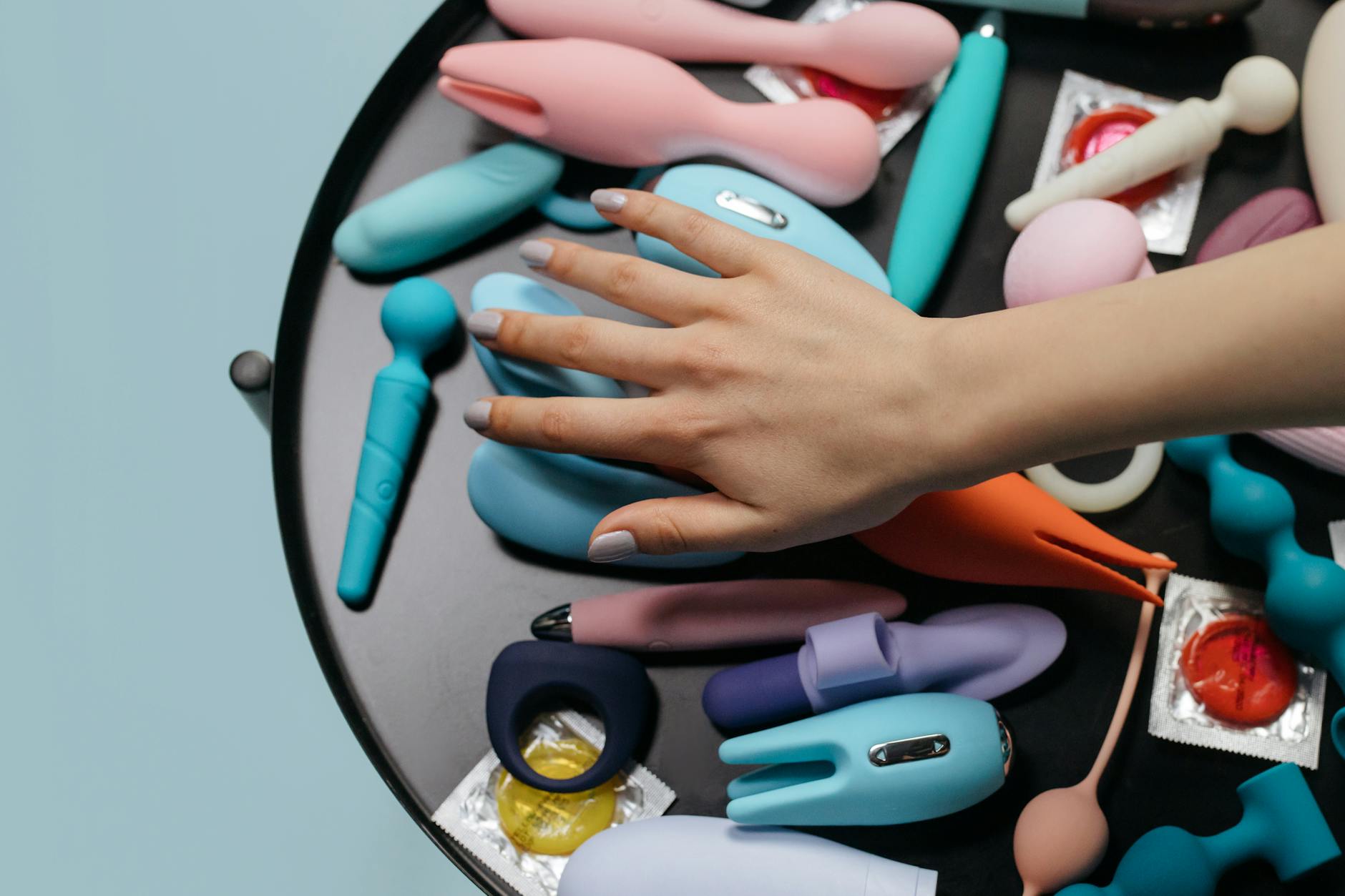 A hand reaching over a variety of colorful sex toys arranged on a table, symbolizing intimacy choices and reconnection.
