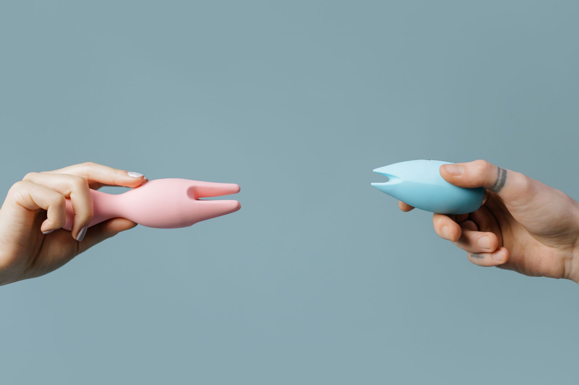 Two hands holding silicone vibrators together in intimate moment