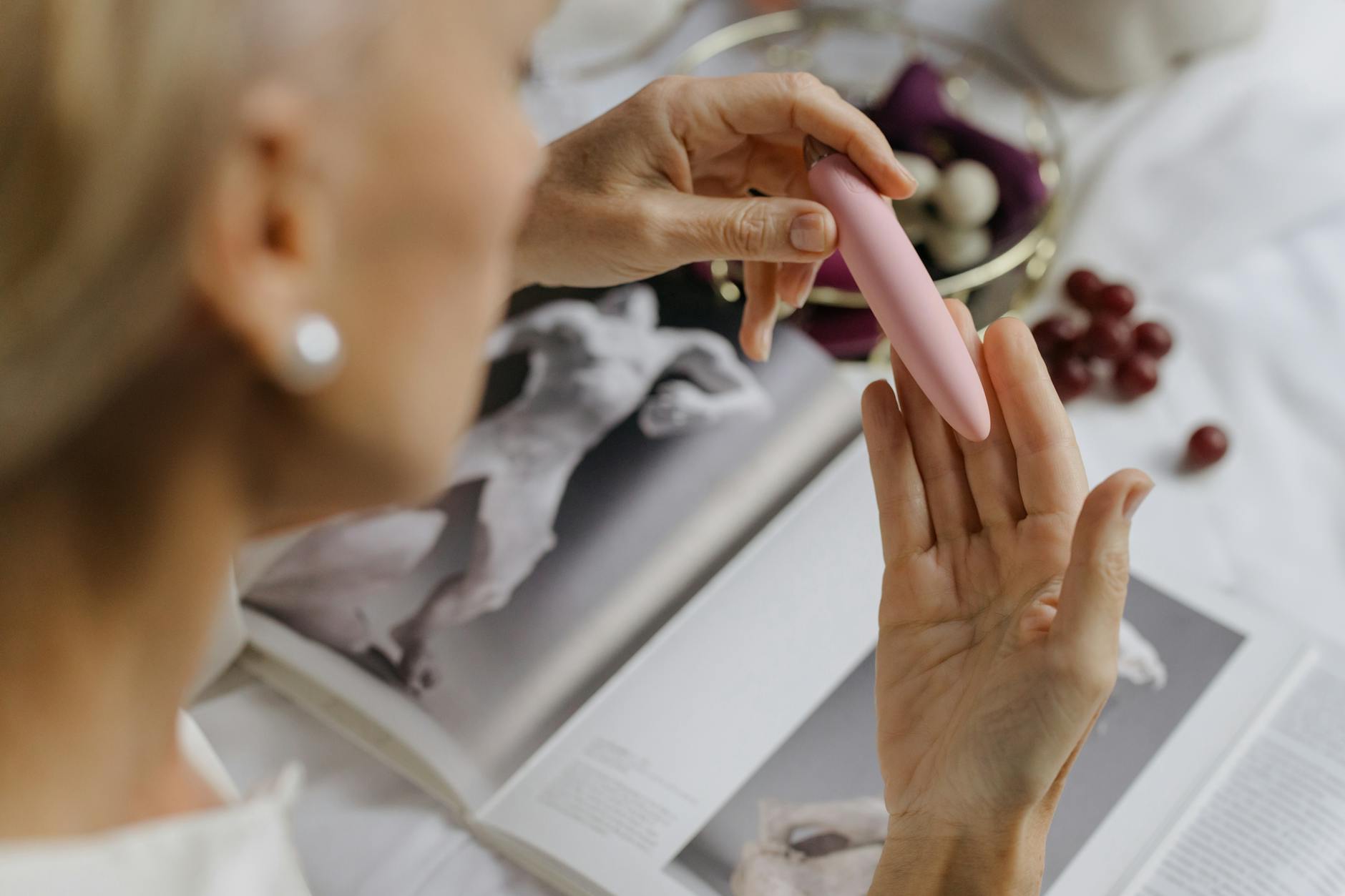 Close-up of a woman holding a pink vibrator with books in the background, symbolizing intimate reconnection and personal empowerment