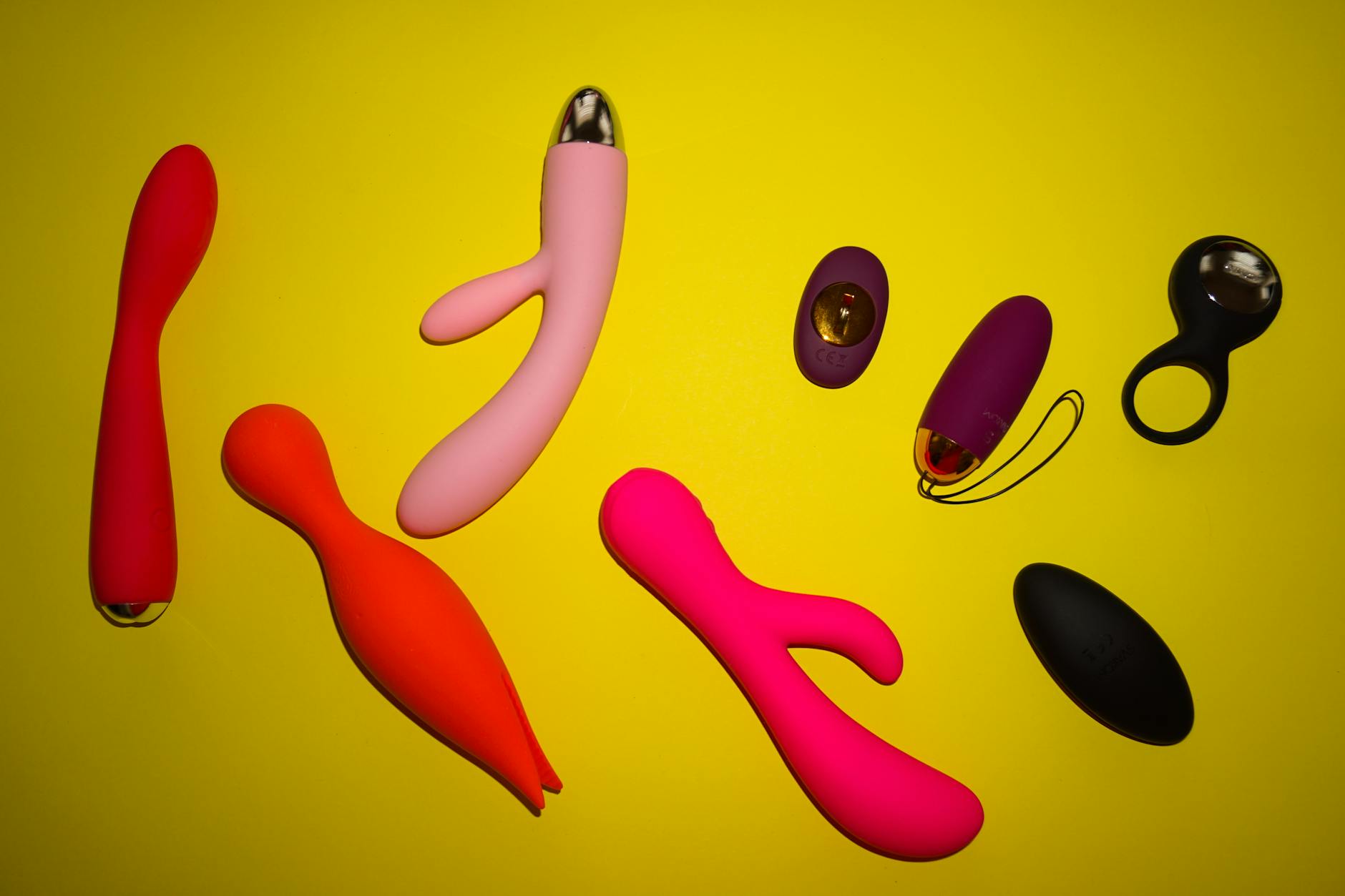 Vibrant colorful sex toys arranged on bright yellow surface