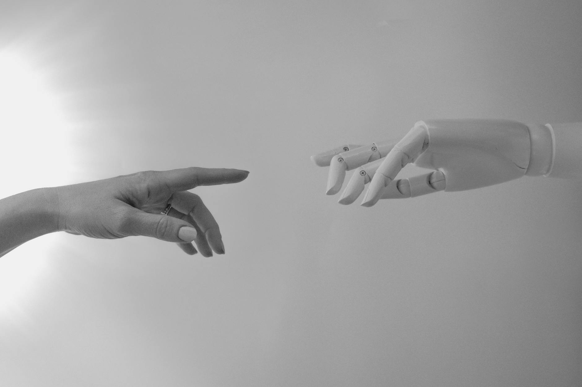 A robotic hand extends toward a human hand, fingers nearly touching, representing the gap between connection and distance.